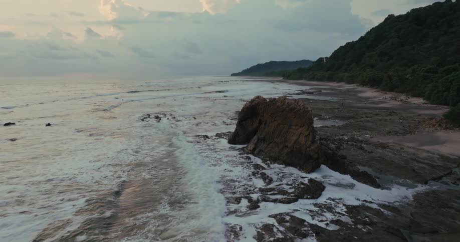 Promontory next to a beach with the ocean to one side and a hill covered by a forest to the other outdoors during dusk or dawn