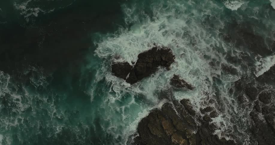 Waves crashing against dark rocks seen from above