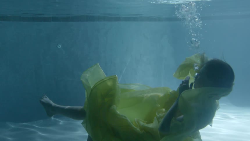 A woman in a yellow dress slowly sinks below the water