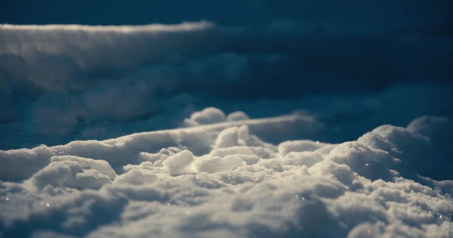 A macro shot focuses on a small pile of white fluffy snow the video shows steam or mist rising from the snow which is illuminated by a warm light against a dark blue background