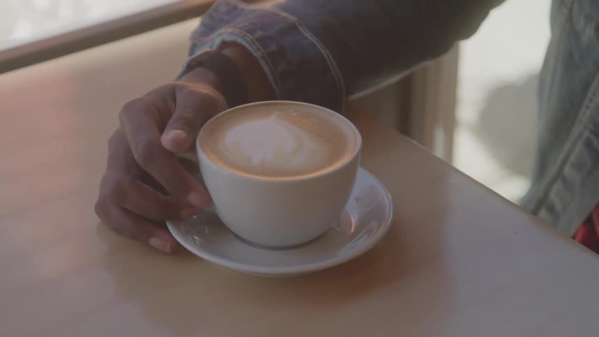 A hand holding on to a cup of cappuccino on a table in front of the person