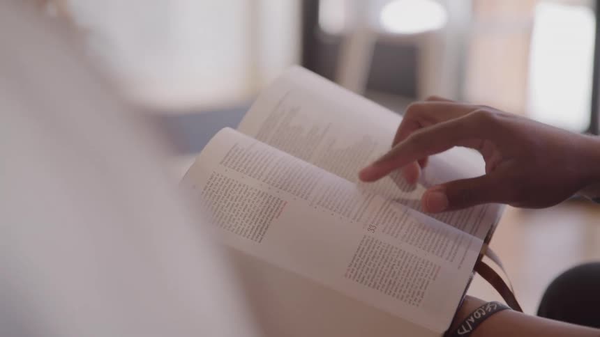 Hands of a black person finger tracking words on a book indoors during day time