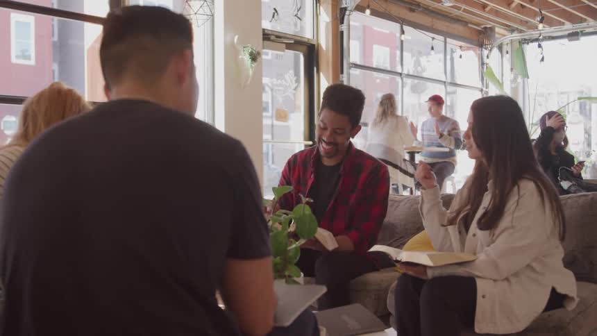A group of people are sitting in a cafe talking and holding books