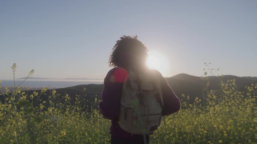 A young black woman walking through a field outdoors during daytime