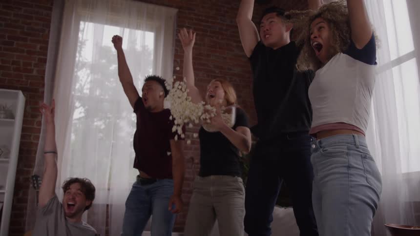 A group of friends watches an event stands up and cheers with their hands in the air