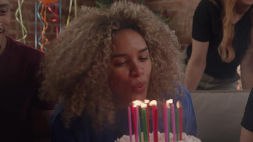 Smiling woman blowing out the candles on a birthday cake with her friends around