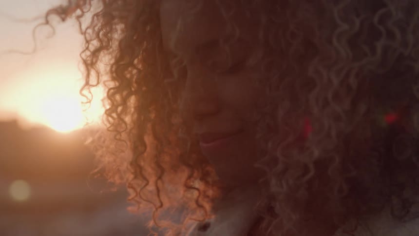 Face of a black woman smiling and standing outdoors during dusk or dawn