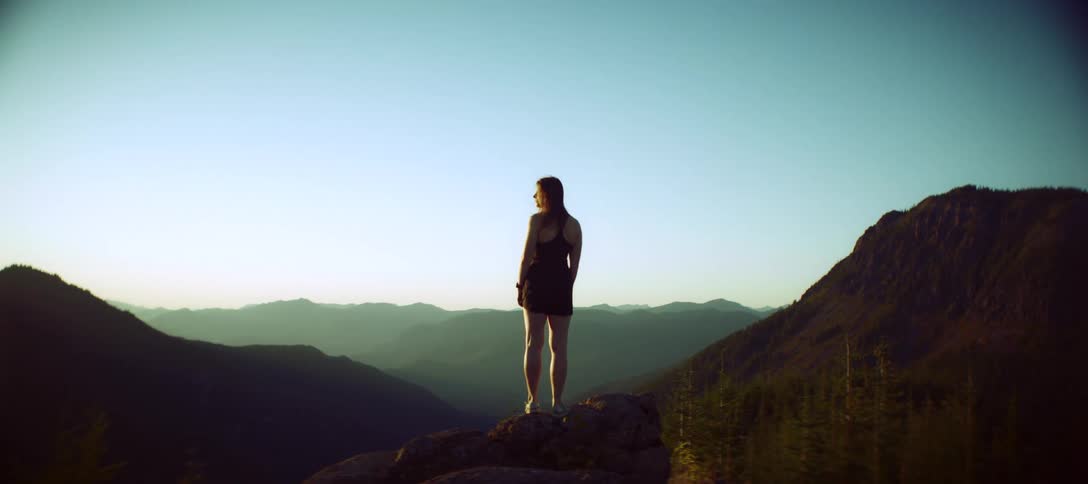 Woman standing on a rock gazes at the sunlit mountainous horizon