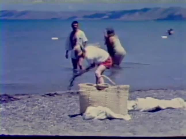 A boy digs in the sand while a family wades in the water