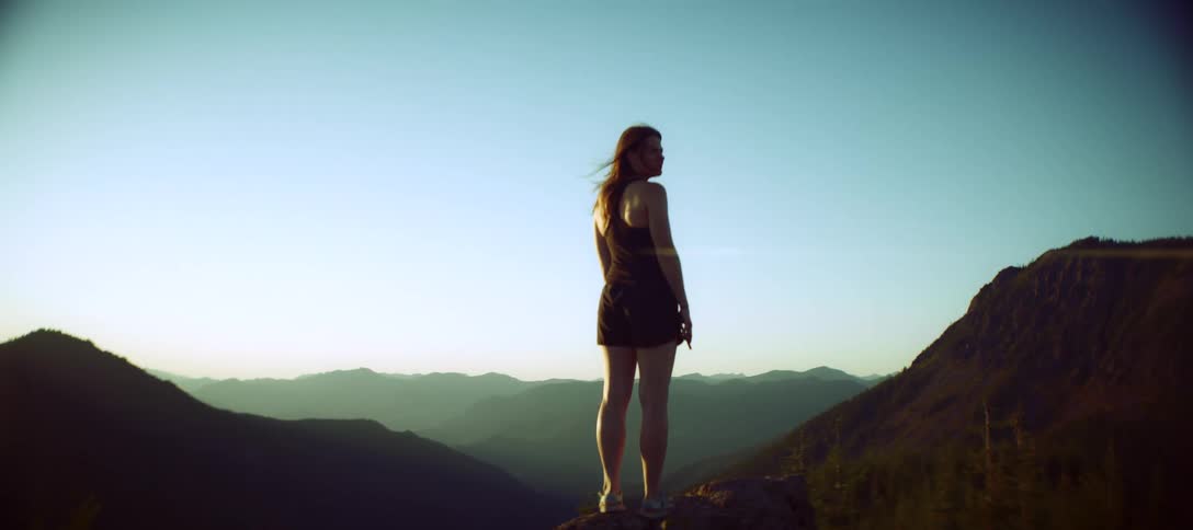 Woman standing on a rock gazes at the mountainous horizon at sunset