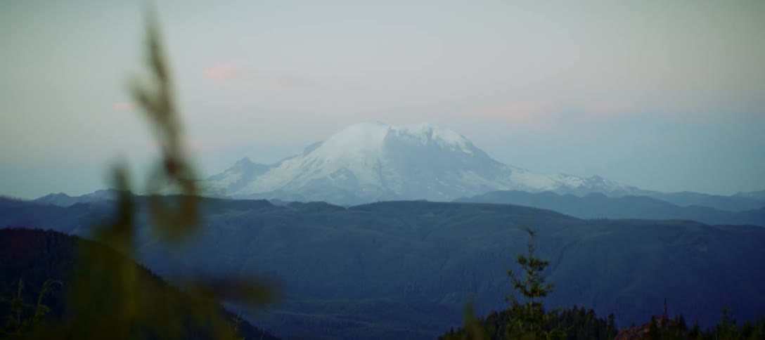 A large mountain with snow on top under a sky with clouds