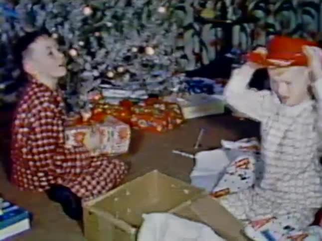 Young boys opening presents at christmas in a vintage scene with one finding a red cowboy hat