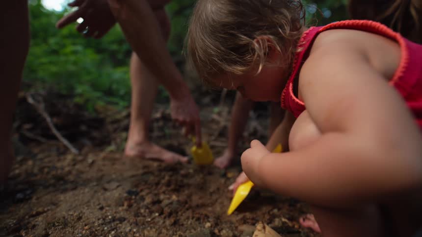 Child digs the soil with a small yellow shovel beside an adult