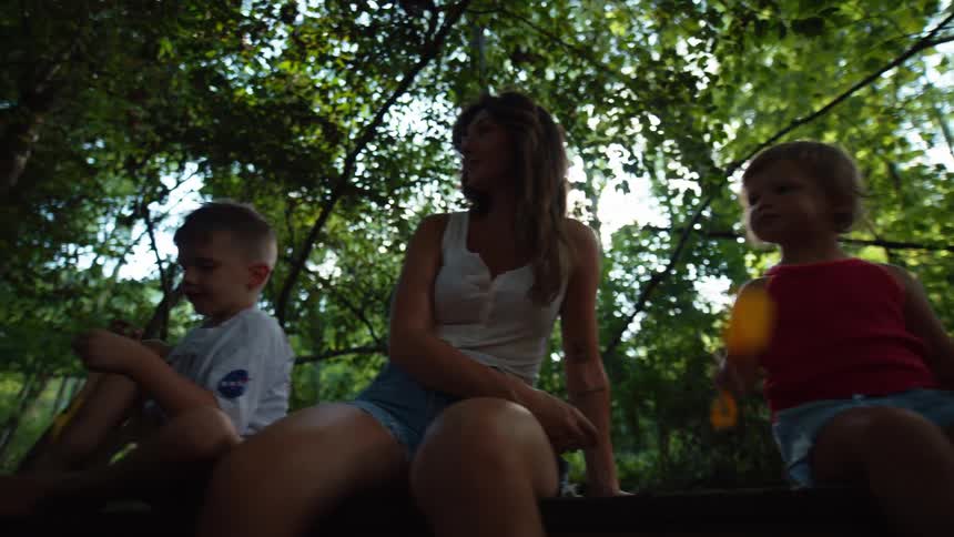 A family of four two children their mother and their father talking to each other as they sit on a tree trunk in a forest
