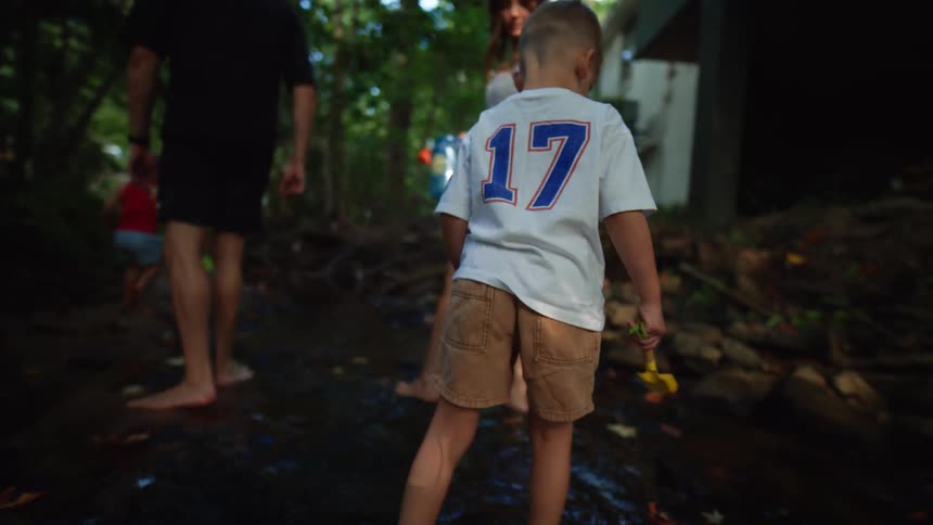 Two people walk away from the camera in a stream while a child walks ahead of them