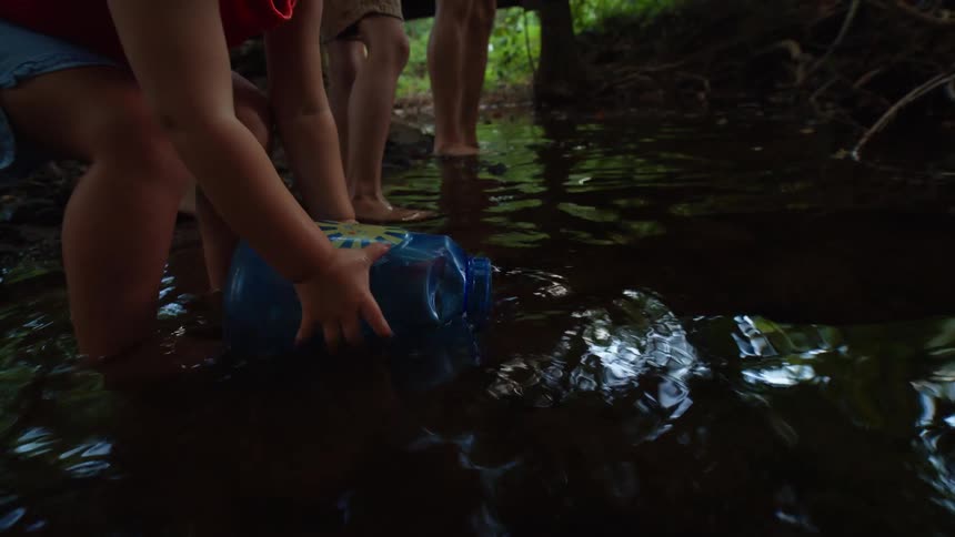Little girl collecting water from a stream with a small gallon