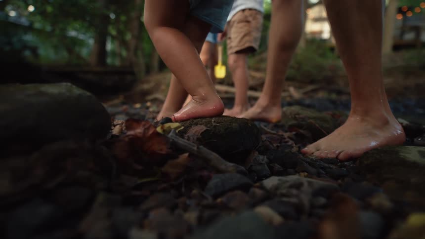 A view from the ground shows the bare feet of a family with a woman and two children and a man standing in a shallow rocky stream