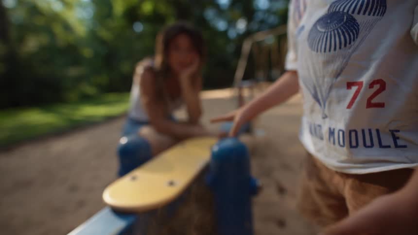 Little boy cleaning his hands of sand and in the background a blurred woman