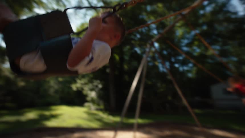 A mother and a father stand on a playground swinging their two kids back and forth on swings