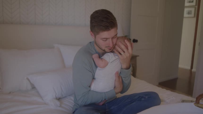 A man holds a baby on a bed and rocks the child back and forth