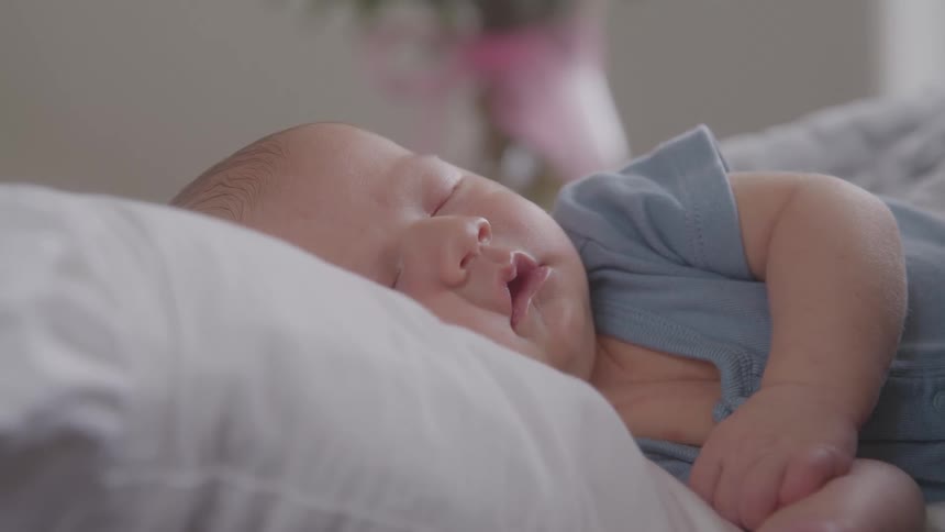 A very close view shows a small baby with closed eyes sleeping on their side on a white pillow