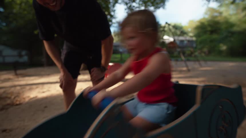A child sits on a toy car while an adult stands behind and watches