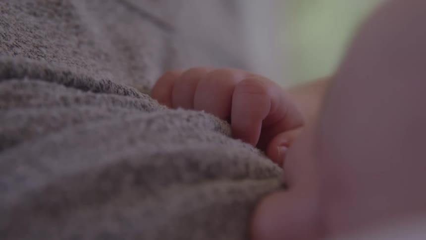 A close static view shows a sleeping babys hand resting on a gray textured blanket
