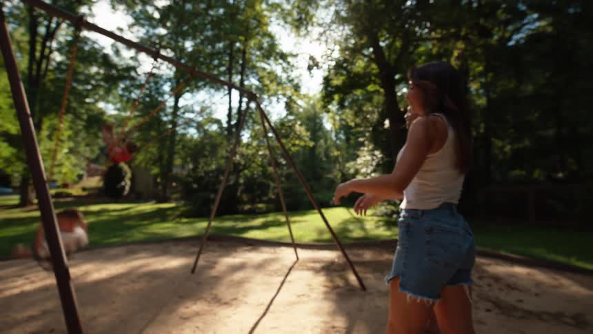 A male and female parent push their children on a swing in an outdoor play area during daytime