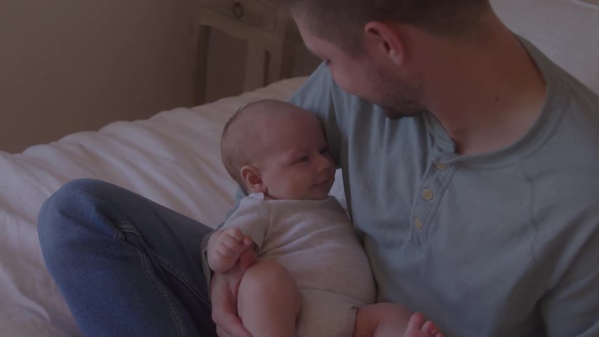 Father sitting on bed with newborn baby on his lap