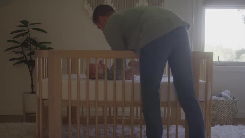 Man carrying a sleeping baby in his arms and putting it on a crib indoors during day time