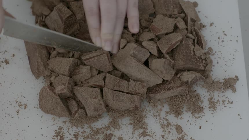 A person holds chocolate pieces and cuts them up