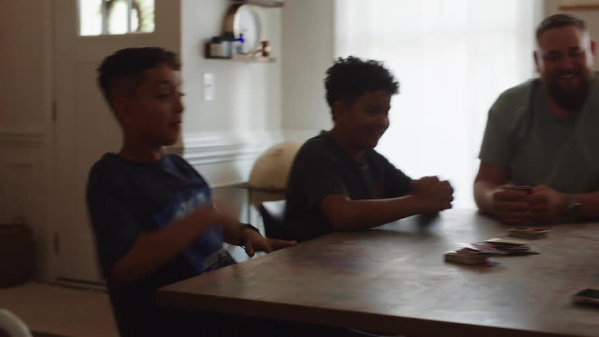 Children clapping their hands while playing cards with adults at the table