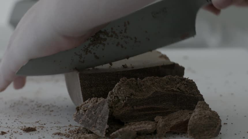 A person is chopping up a block of chocolate