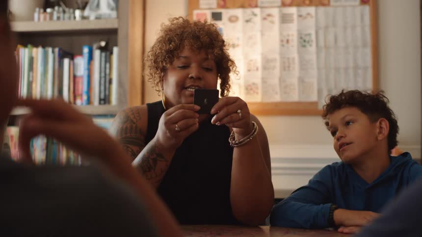 A family group play card games while sitting together at a table indoors during daytime