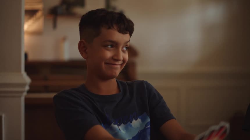 Close up of a male teenager playing a card game with family while sitting at a table indoors