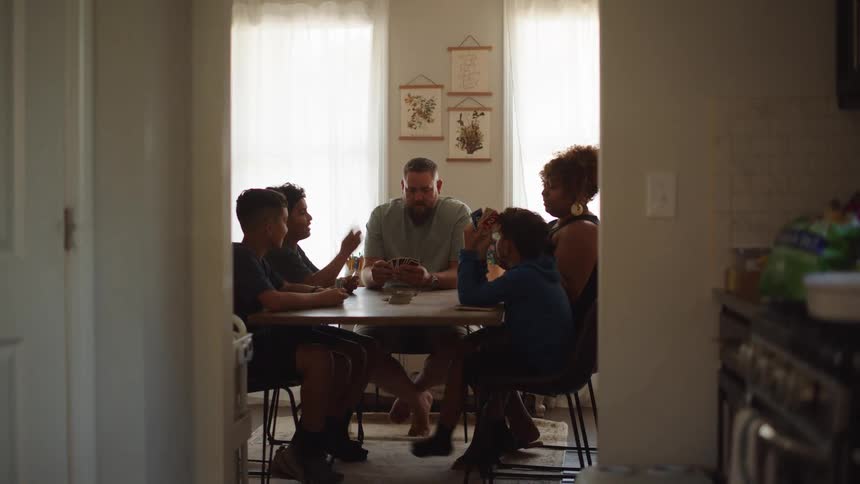 Family gathered around the table plays cards in a room lit by natural light