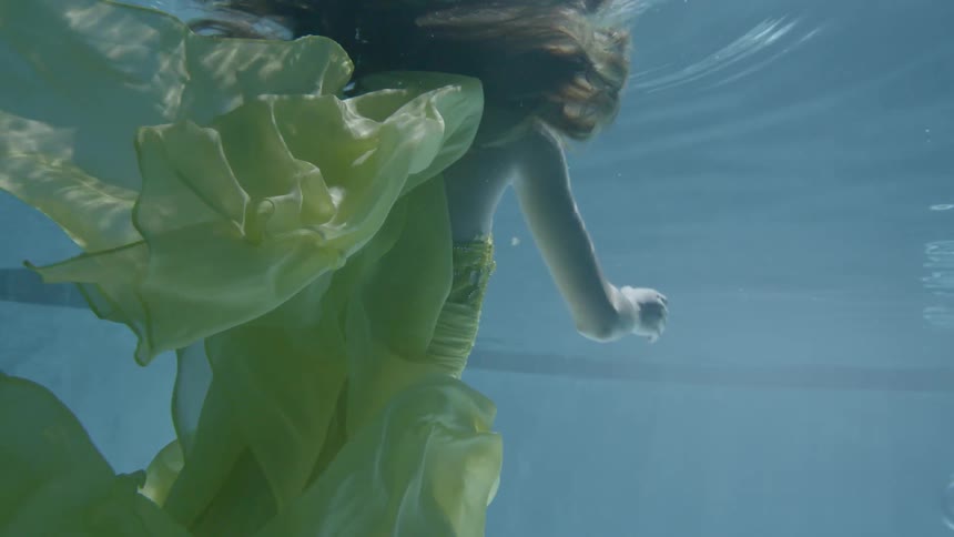 A woman wearing a yellow dress floats in the water waving her arms