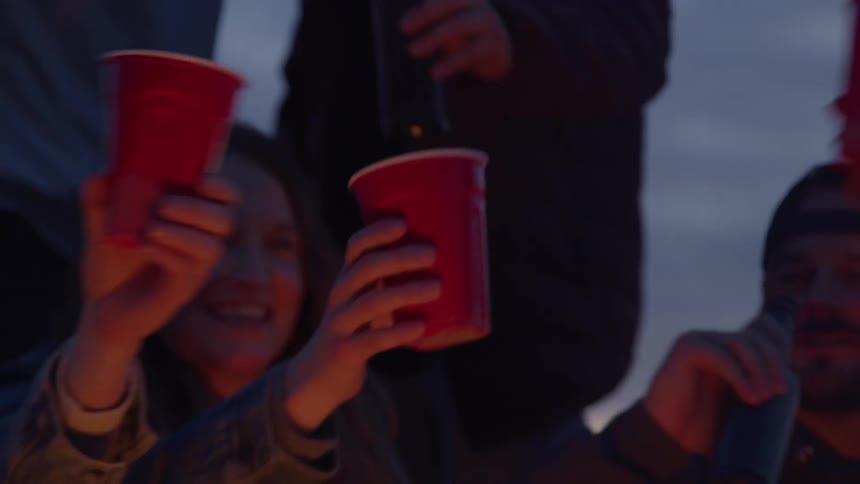 A group of people cheers by clinking their cups and bottles together