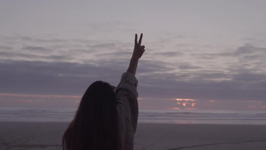 Woman on the beach in the late afternoon raising her hand making a peace sign