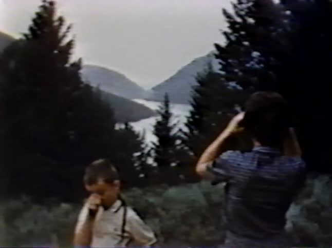 A child looks on as a woman views a lake with binoculars