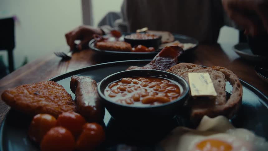 A person putting a fork next to a plate with breakfast food while eating in another plate full of breakfast food