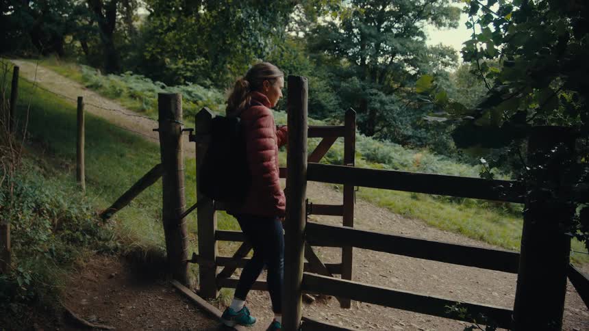 A hiker with a backpack is standing next to a wooden fence on a dirt path in a forest the person is looking over the fence taking in the scenery