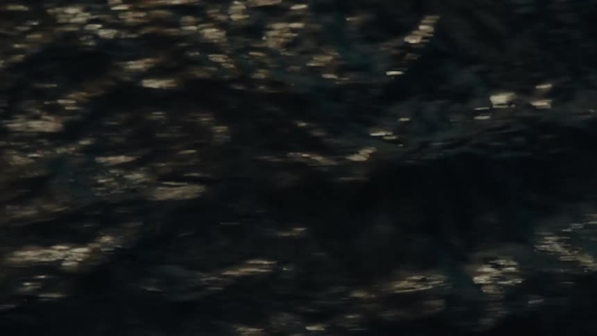 Glints of sunlight reflect on the moving surface of a dark body of water creating bright shimmering patterns on the waves
