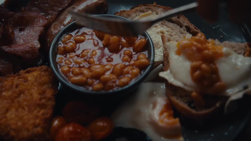 A hand spreads baked beans on bread ready to eat from a plate