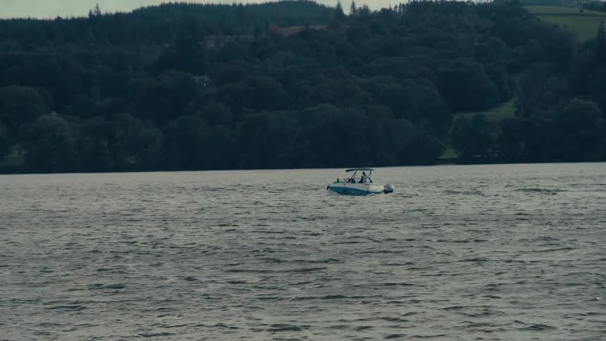 A motorboat moves from left to right across a large body of water the boat is in the midground with a forested hillside in the background