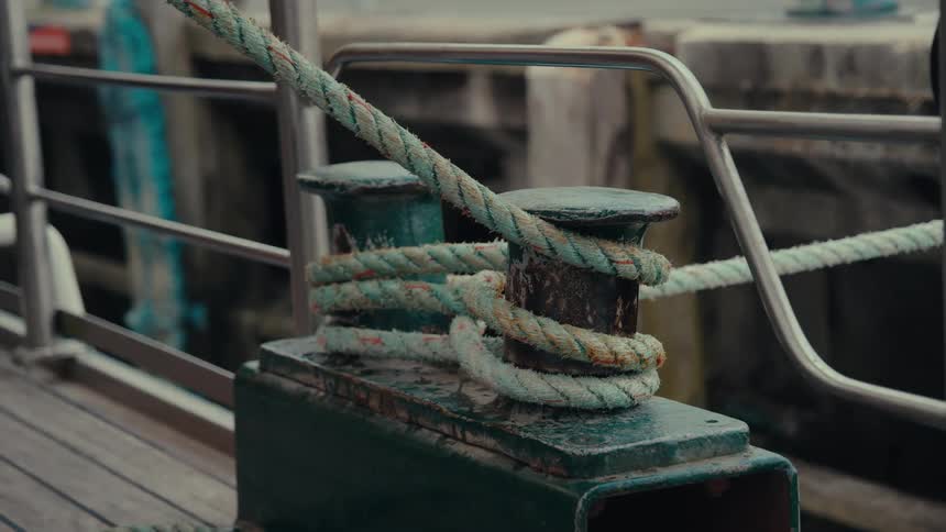 A persons hand wraps a rope around a metal cleat on a boat deck