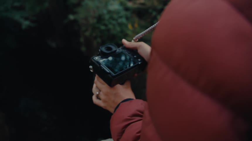 Close up of a young woman taking photos with a camera while hiking in a woodland area during daytime
