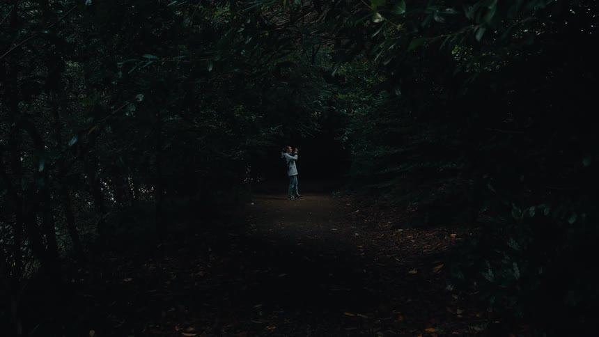Person takes a photo on a trail surrounded by dark trees