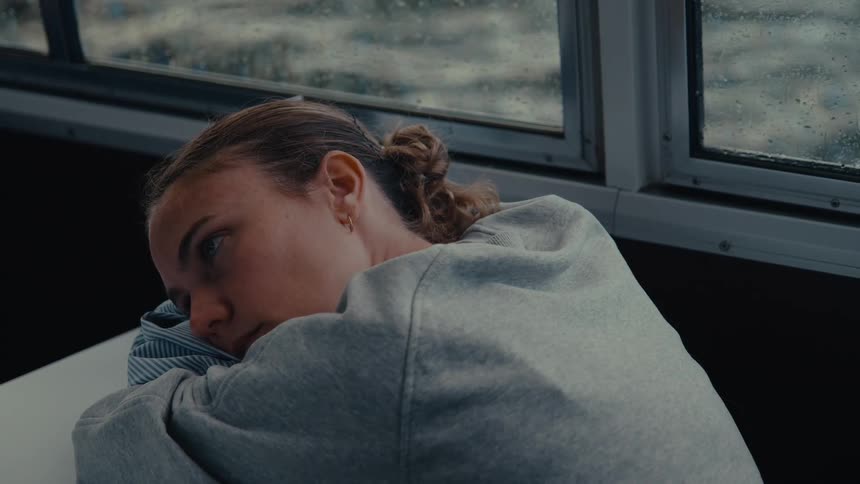 Close up of a young female teenager resting her head on a surface while in a moving transportation vehicle during daytime