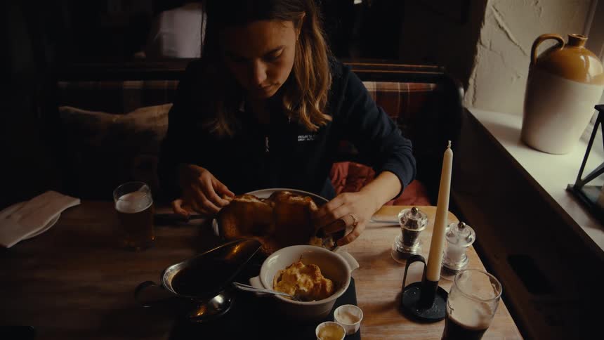 A woman seasons her food with a pepper grinder in a restaurant